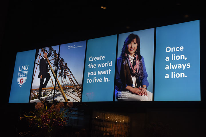 A large LED billboard with two photos of alumni, the LMU logo, the words Create the world you want to live in, and the words Once a lion always a lion