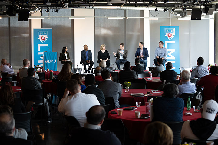 Several guest speakers having a conversation on a stage with LMU branded banners on either side