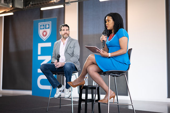 Two people seated on a stage speaking to an audience