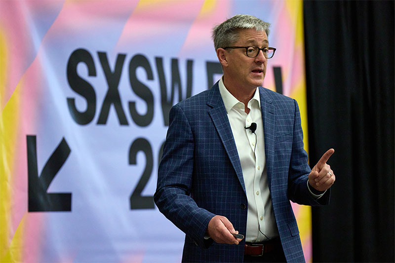 President Timothy Law Snyder speaking to an audience from a stage with the SXSW logo behind him
